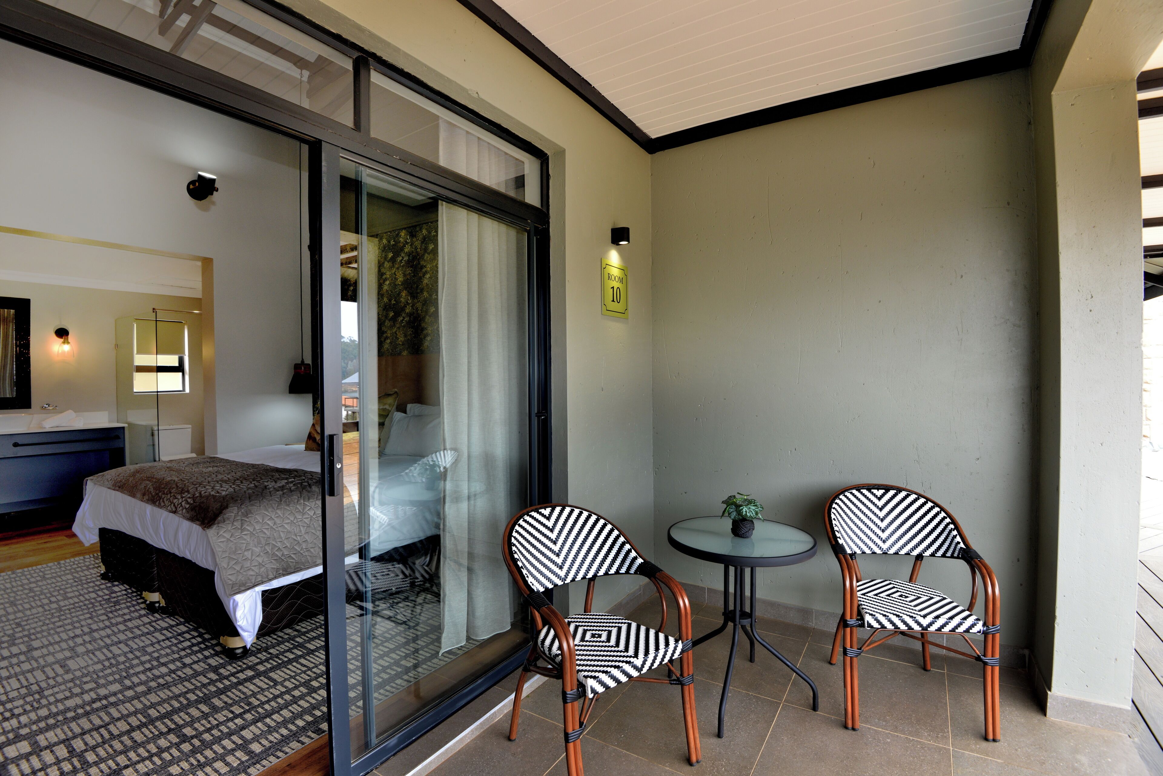 A hotel room with a bed, a glass door leading to a balcony, and two chairs.