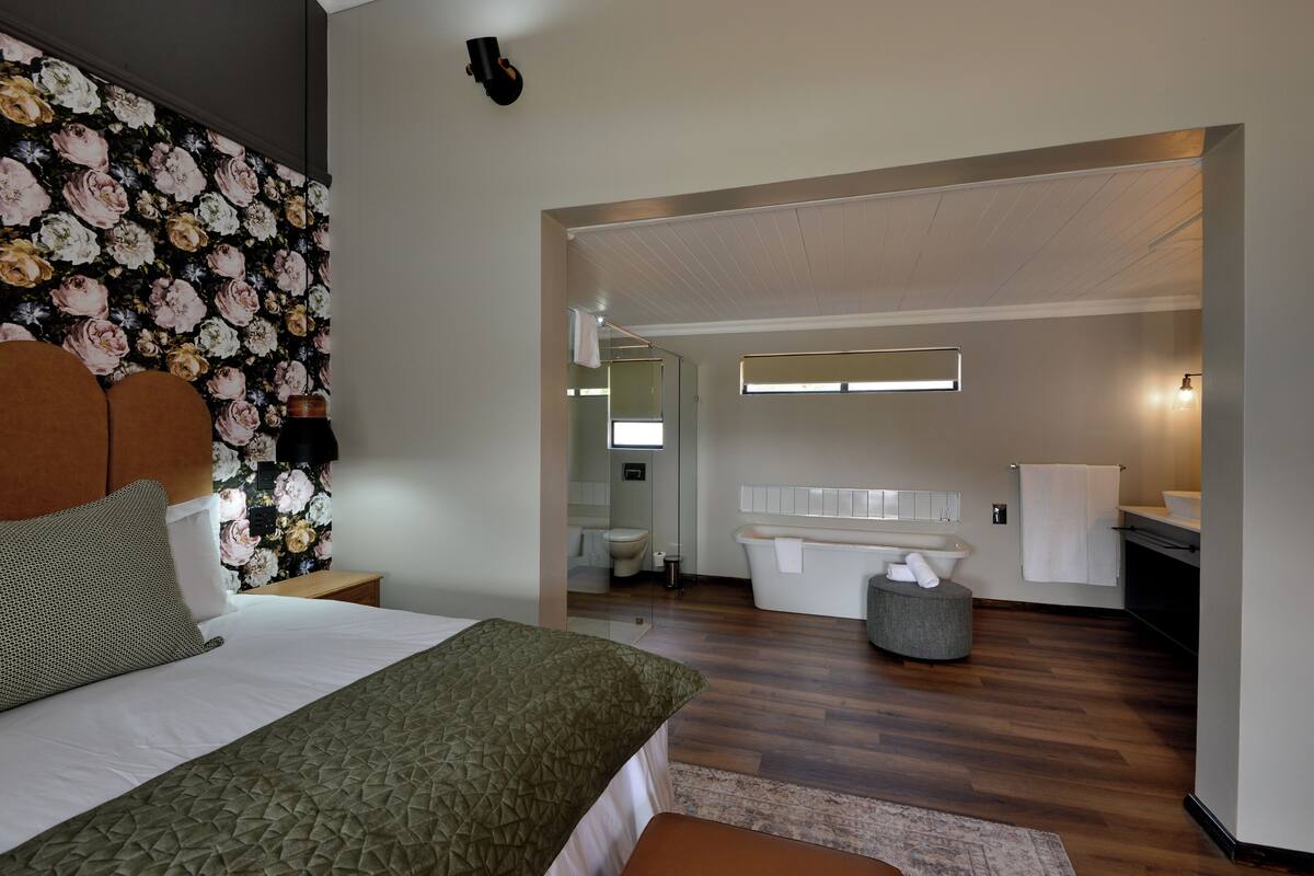 A modern hotel room with a large bed, a bathroom with a bathtub, and a kitchenette area.