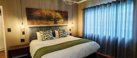 A bedroom with a large bed, a painting on the wall, and a window with curtains.