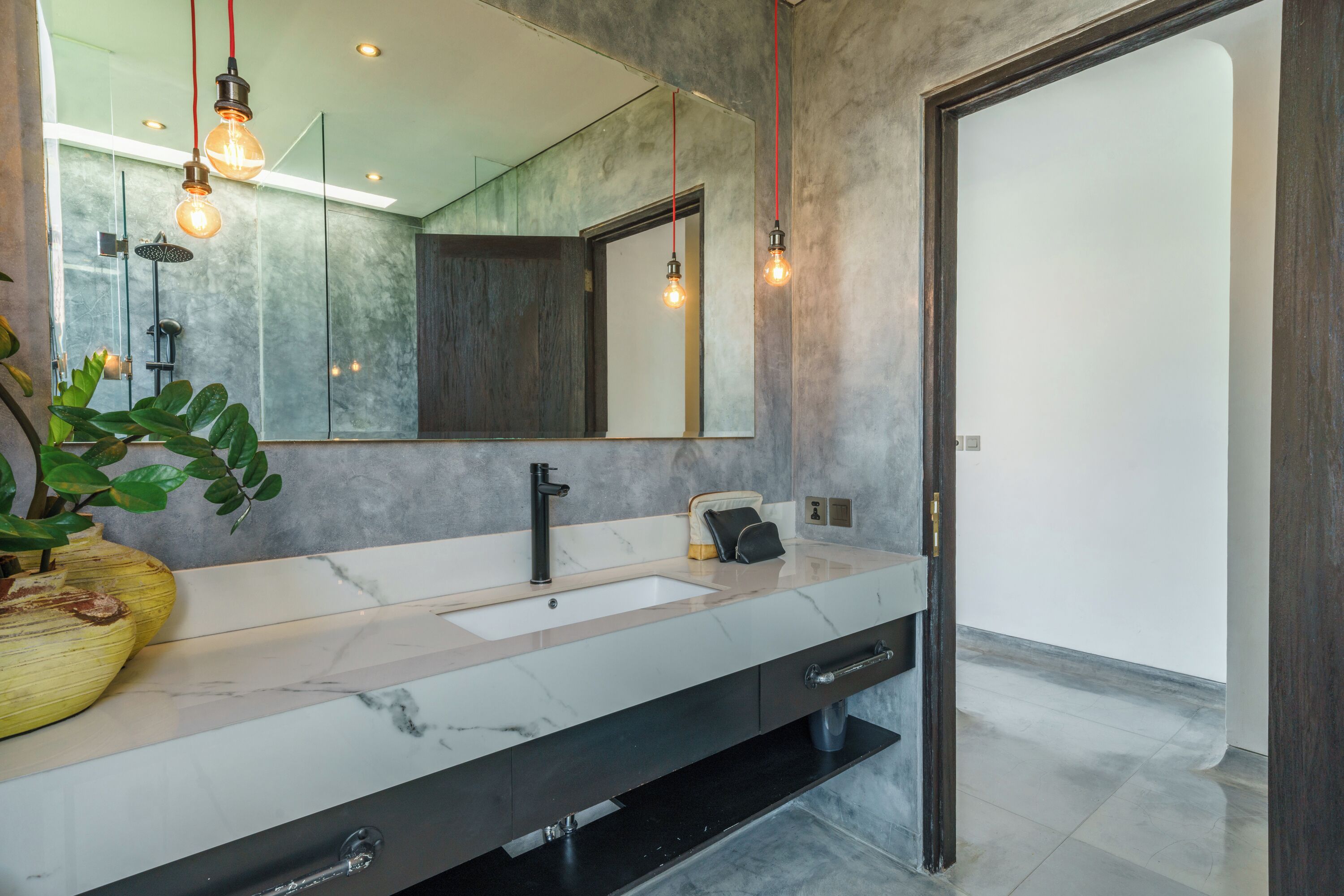 A modern bathroom with a marble sink, black faucet, and a large mirror. There are two pendant lights hanging above the sink.