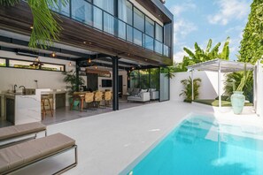Une maison moderne dotée d’une piscine, d’un espace extérieur aménagé et d’une grande cuisine.