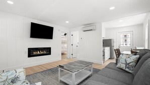 A modern living room with a fireplace, a flat-screen TV, and a dining area with a table and chairs.