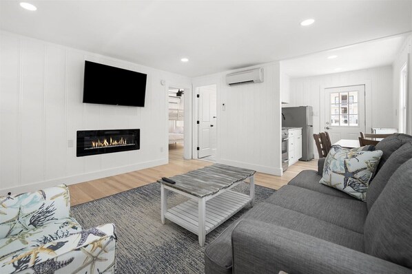 A modern living room with a fireplace, a flat-screen TV, and a dining area with a table and chairs.
