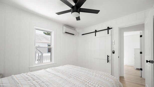 Un dormitorio con una cama, ventilador de techo, ventana y puerta.