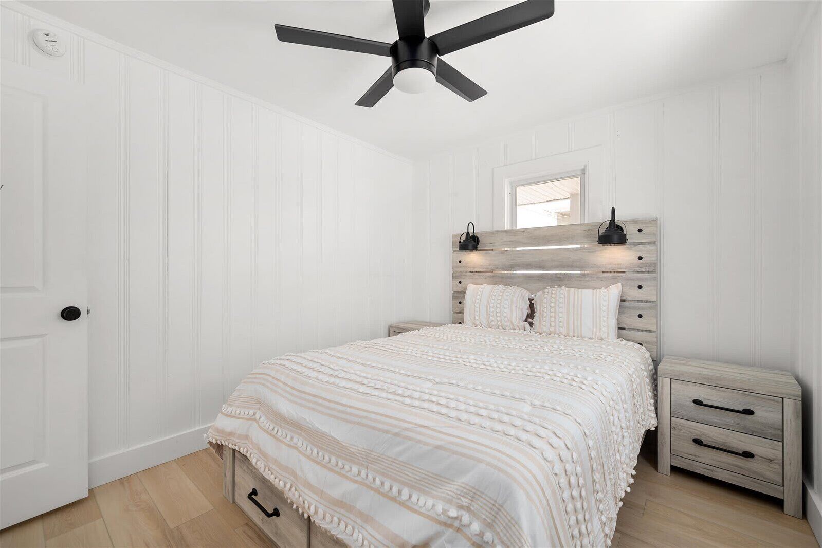 A bedroom with a bed, bedside tables, a ceiling fan, and a door.