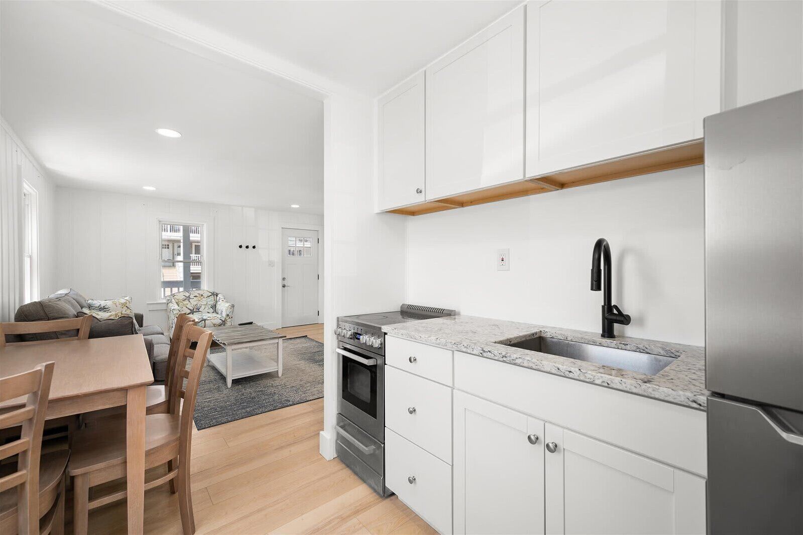 A modern kitchen with white cabinetry, a built-in oven, a stainless steel refrigerator, and a granite countertop.