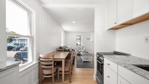A modern kitchen with white cabinetry, a wooden dining table, and a view of the street outside.