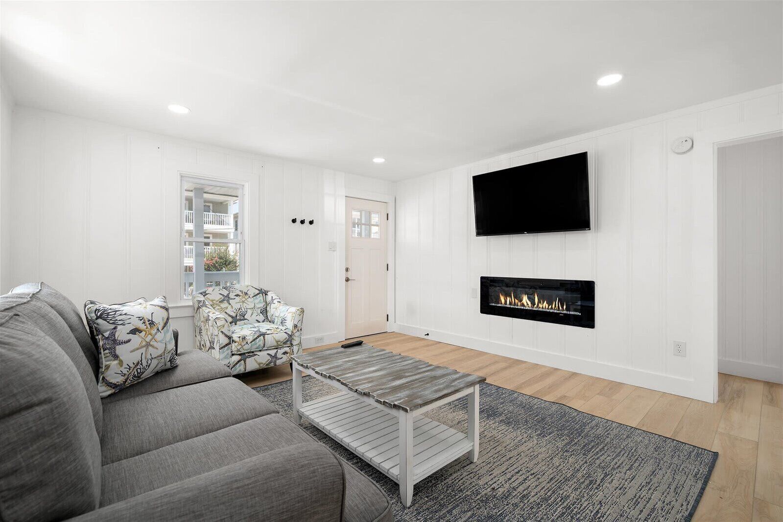 A modern living room with a grey sofa, patterned armchair, and a flat-screen TV mounted above a fireplace.