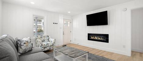 A modern living room with a grey sofa, patterned armchair, and a flat-screen TV mounted above a fireplace.