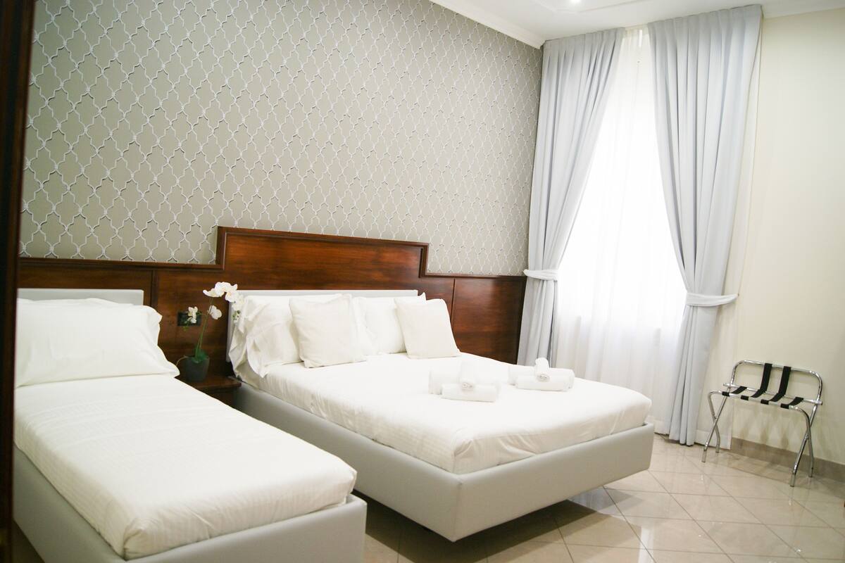 Ein Hotelzimmer mit zwei Betten, einem Holzkopfstück, einem kleinen Tisch mit einer Pflanze und einem Stuhl.