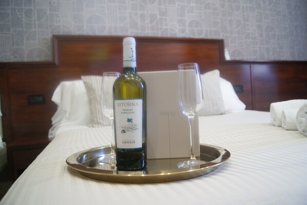 Habitación de hotel con una cama, una bandeja con una botella de vino y una copa, y un menú en la cabecera.
