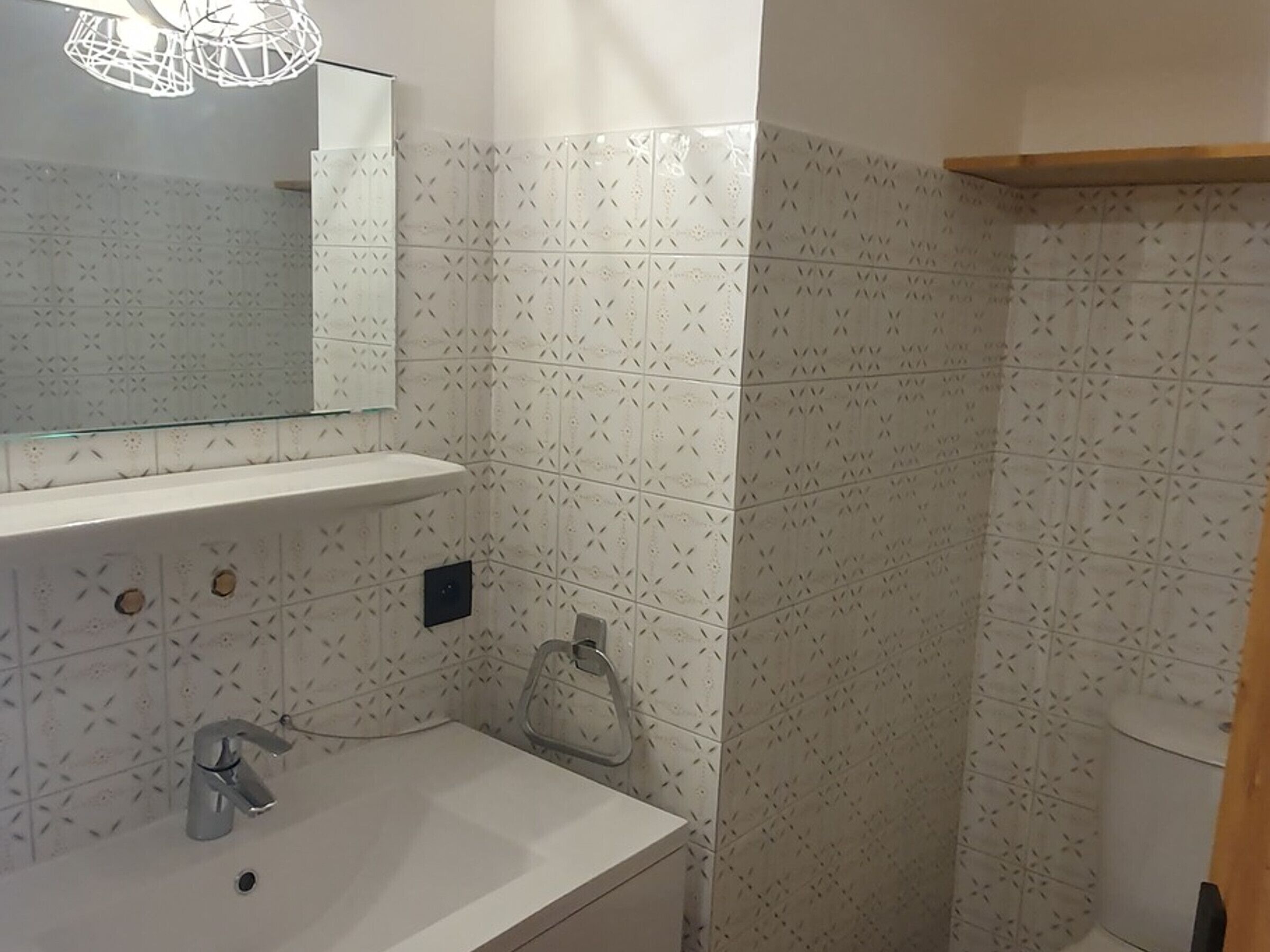 A bathroom with a white sink, a mirror above it, and patterned tiles on the walls.