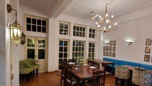 A dining area with a wooden table and chairs, a chandelier, and a blue accent wall. - Mango Tree Courtyard Dehradun (Dehradun)