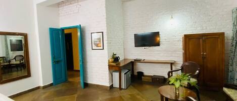 A living room with a white brick wall, a ceiling fan, a TV mounted on the wall, a wooden table, and a chair.