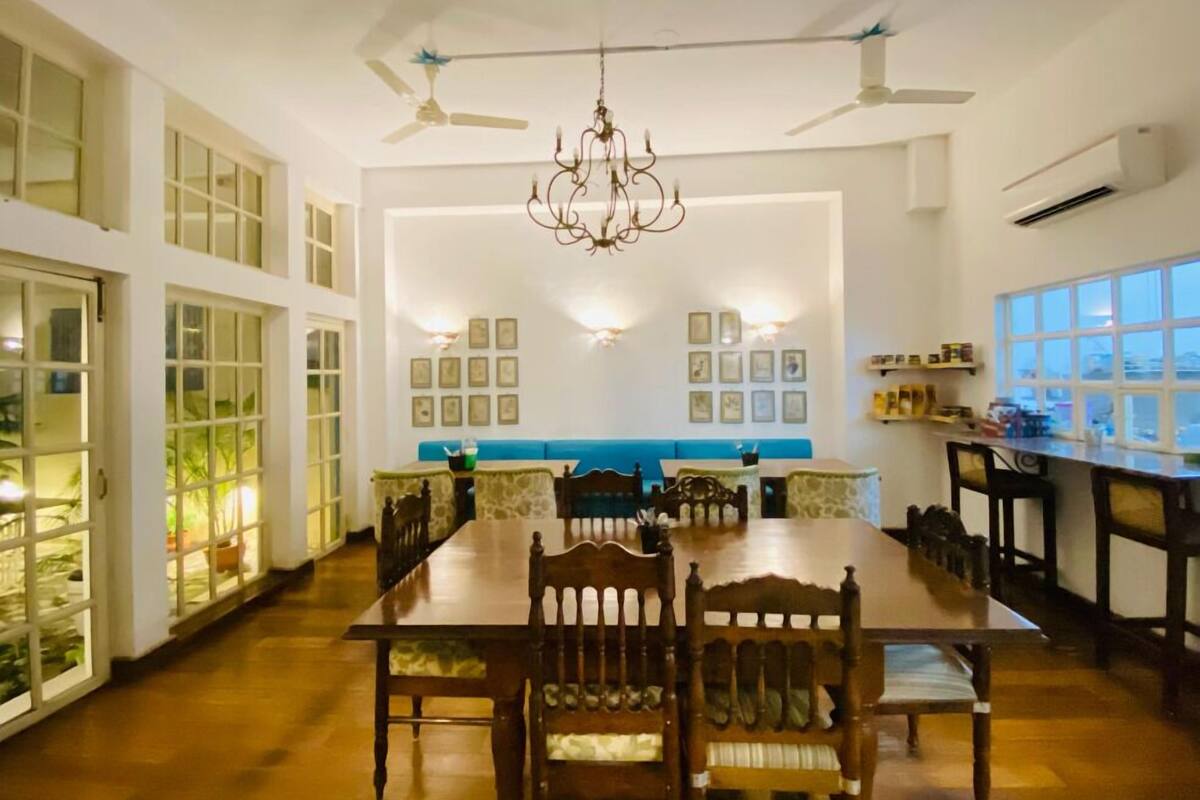 A dining area with a long wooden table, chairs, a chandelier, ceiling fans, and wall-mounted lights.