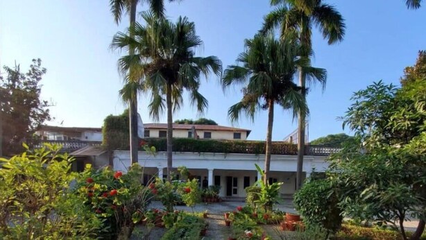 A building with a garden in front, surrounded by palm trees. - Mango Tree Courtyard Dehradun (Dehradun)