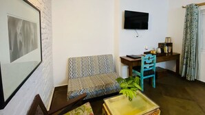 A living room with a sofa, a small table, a television mounted on the wall, and a desk with a chair. - Mango Tree Courtyard Dehradun (Dehradun)