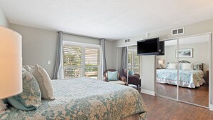Un dormitorio con una cama grande, televisor, una silla y puerta corrediza de vidrio al exterior.