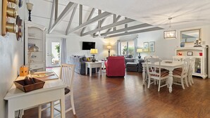 Un amplio salón con piso de madera, una mesa de comedor con sillas, un sillón rojo y un sofá.