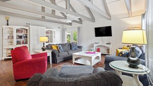 Un salón con un sillón rojo, un sofá gris y una mesa de centro blanca. Se observa una estantería, un televisor de pantalla plana y una lámpara.
