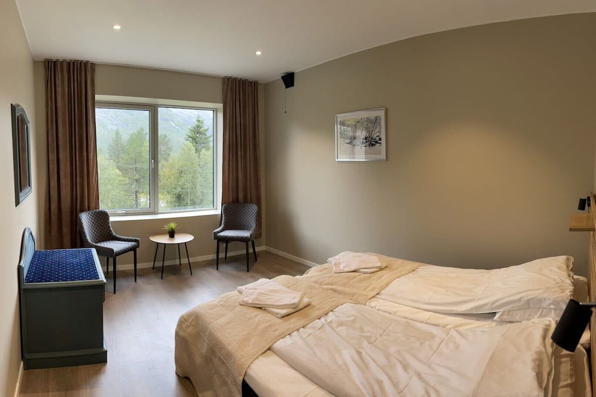A hotel room with a bed, two chairs, a small table, and a window with curtains.