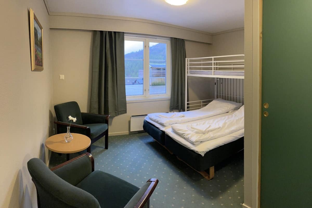 A hotel room with a bunk bed, a desk with a chair, a small round table, and a window with curtains.