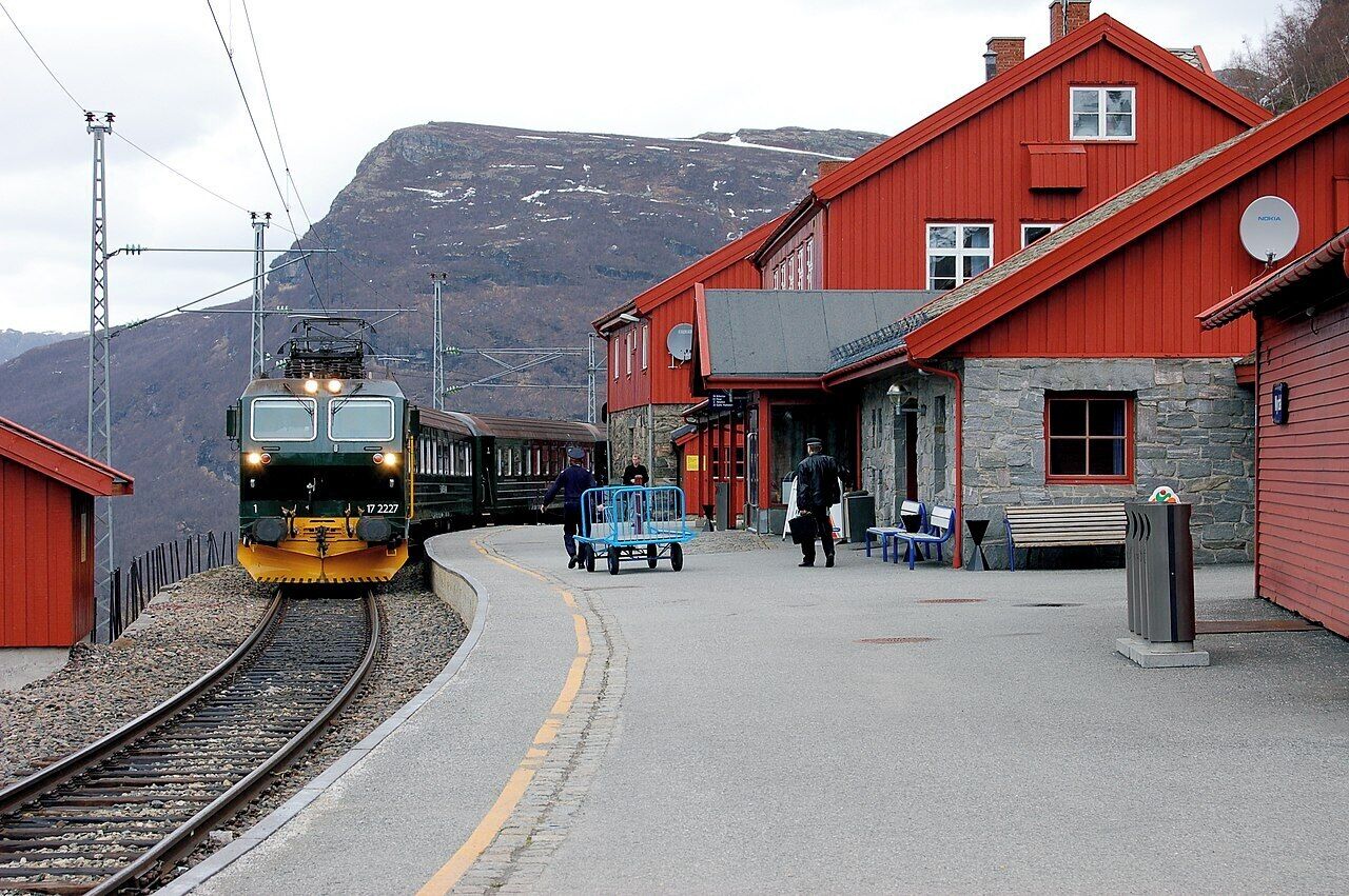 A train station with a red building, a platform, and a mountainous background.