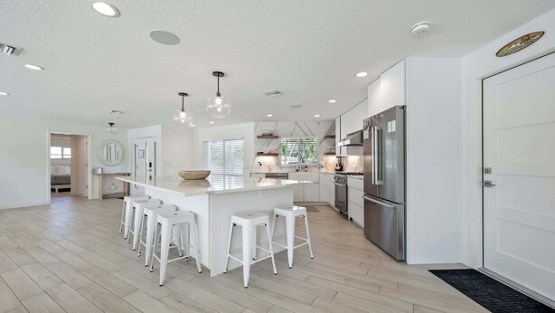 A modern kitchen with a central island, white bar stools, stainless steel appliances, and recessed lighting. - Luxury Beachside 4BR/3BA Waterfront Home (Cocoa Beach)