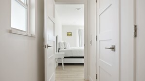 A narrow hallway leading to a bedroom with a bed, a desk, and a window. - Luxury Beachside 4BR/3BA Waterfront Home (Cocoa Beach)