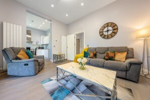 A modern living room with a grey sofa set, a marble coffee table, and a wall clock.