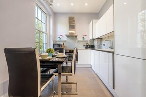A modern kitchen with white cabinets, a stainless steel range hood, and a dining area with a black table and chairs.