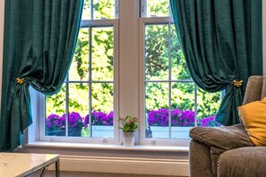 A room with a window, curtains, a chair, and a small potted plant.