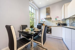 Una cocina moderna con gabinetes blancos, encimera negra y una zona de comedor con sillas blanco y negro.