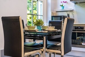 A modern dining area with a glass table, black chairs, and a potted plant. - Spacious 2-Bedroom Apartment in Greater London (London)