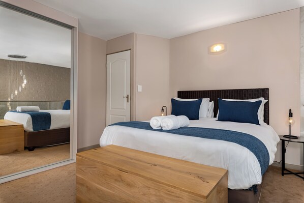 A modern hotel room with a large bed, a wooden bench, a mirror, and a small table. - Harbour Terrace 29 (Cape Town)