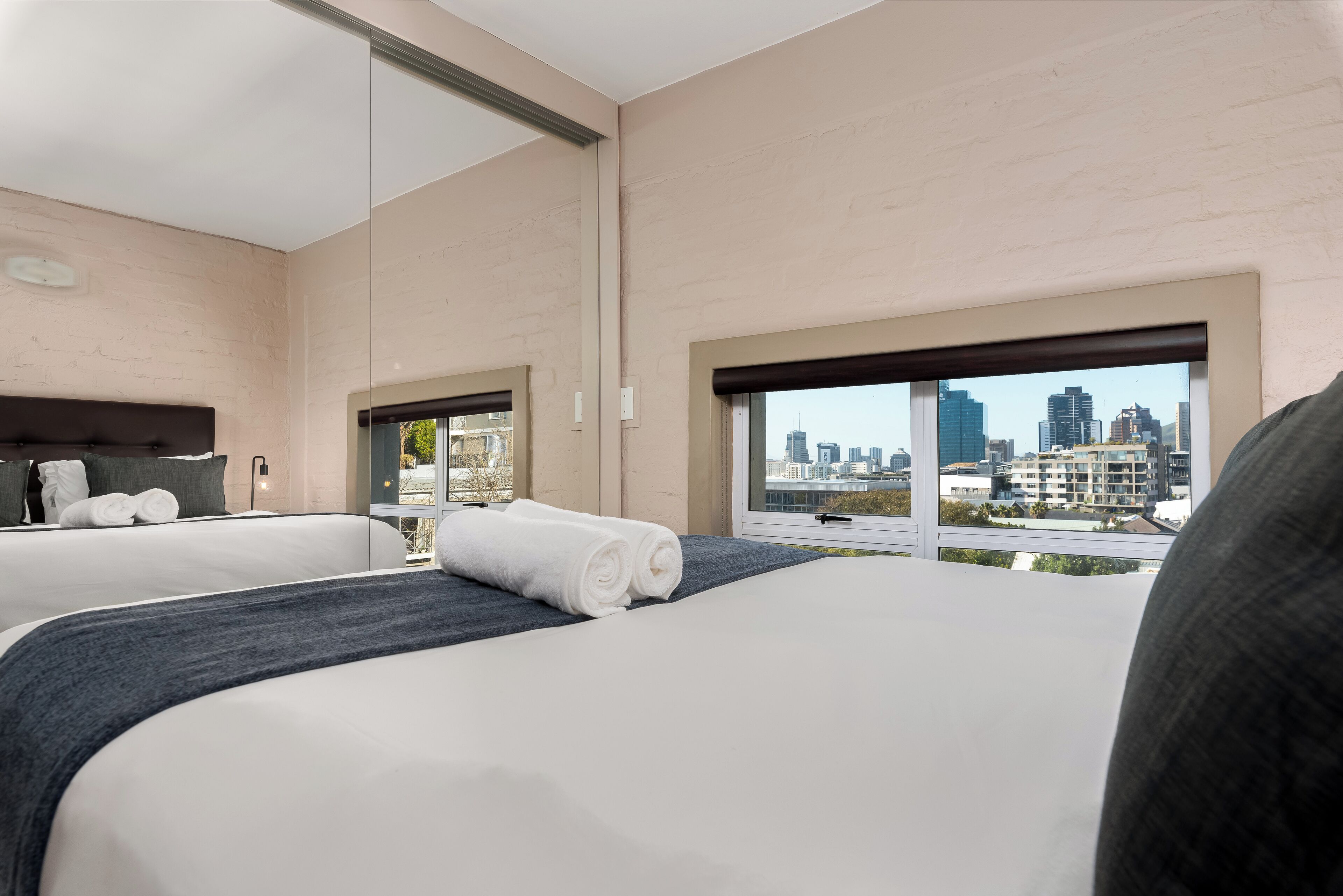 A hotel room with two beds, a city view, and a large window.