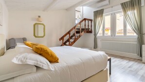 A bedroom with a bed, a wooden staircase, a window with curtains, and a radiator. - Salvemini Home in Firenze (Florence)