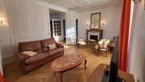 Un salón amplio con un sofá de cuero marrón, un reposapiés estampado y una chimenea con un espejo encima.