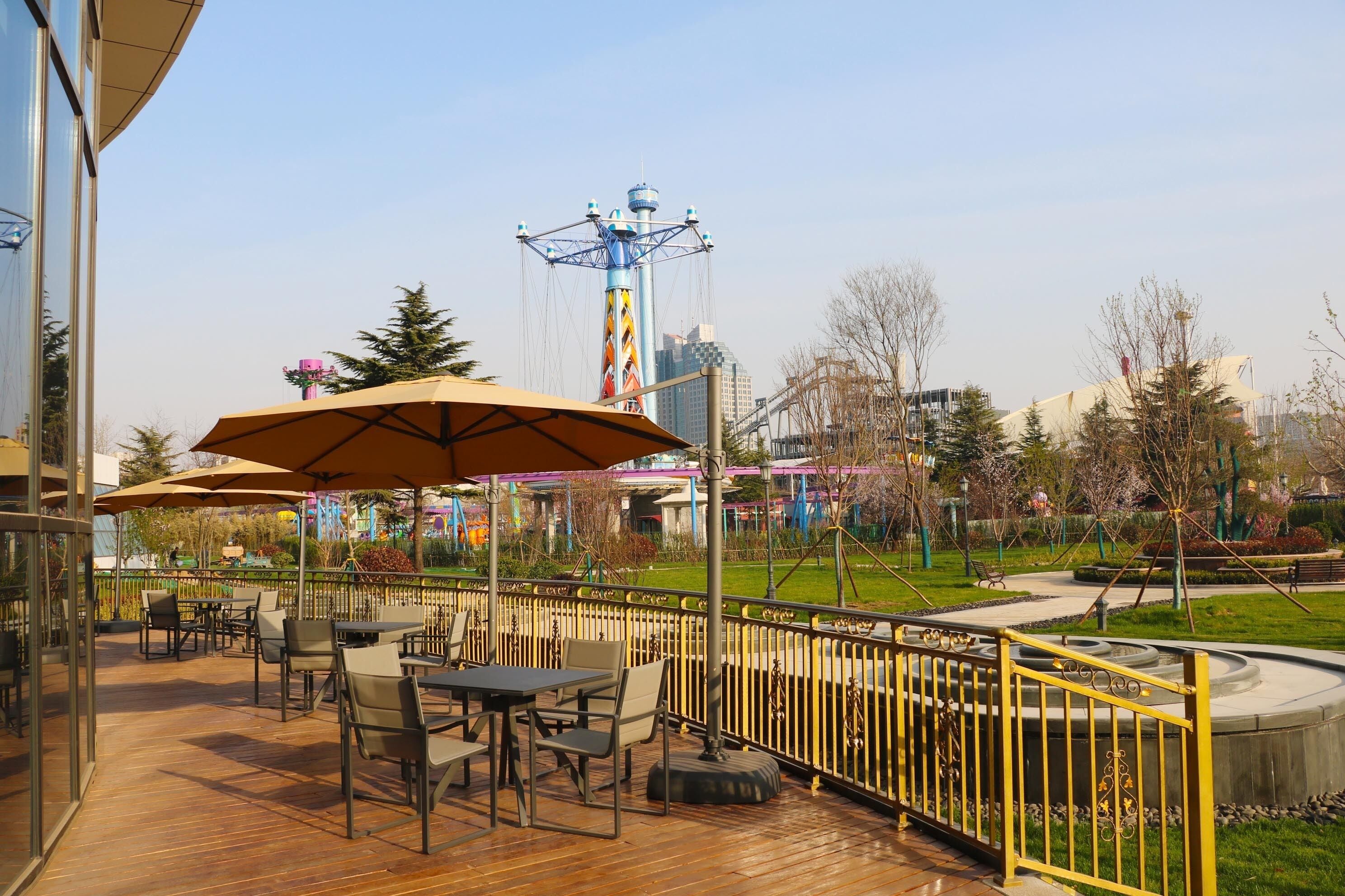 An outdoor seating area with tables and chairs, a yellow railing, and a Ferris wheel in the background.