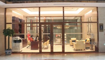 Un moderno vestíbulo de hotel con mostrador de recepción, zona de estar y un amplio acceso por puerta de vidrio.