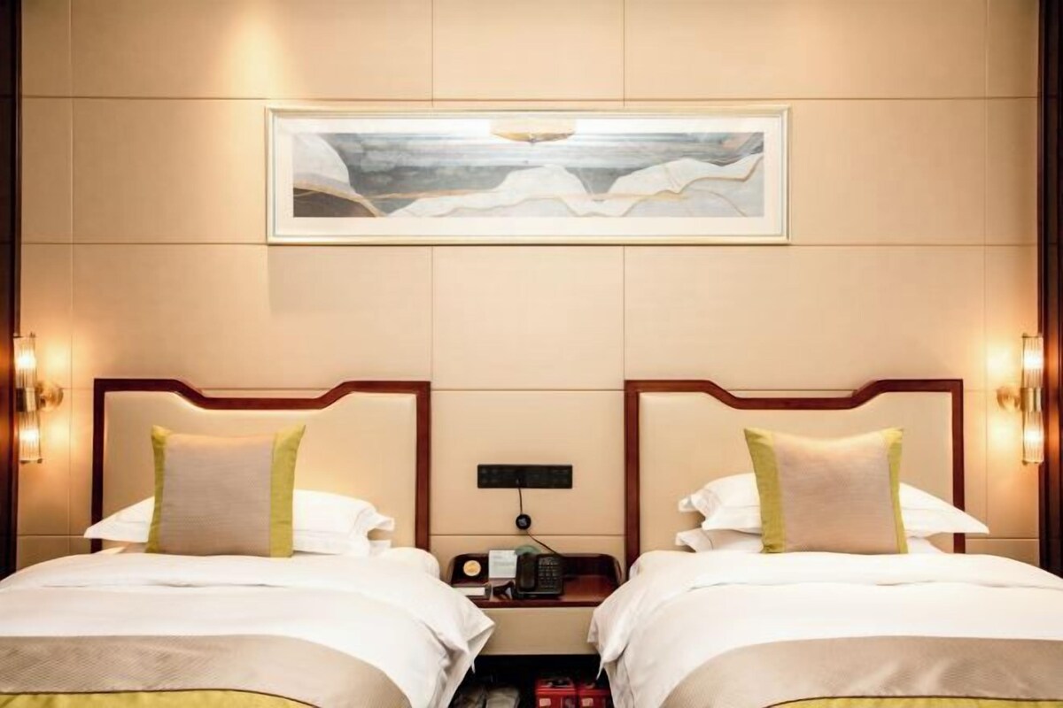 A hotel room with two beds, a painting on the wall, and bedside lamps.