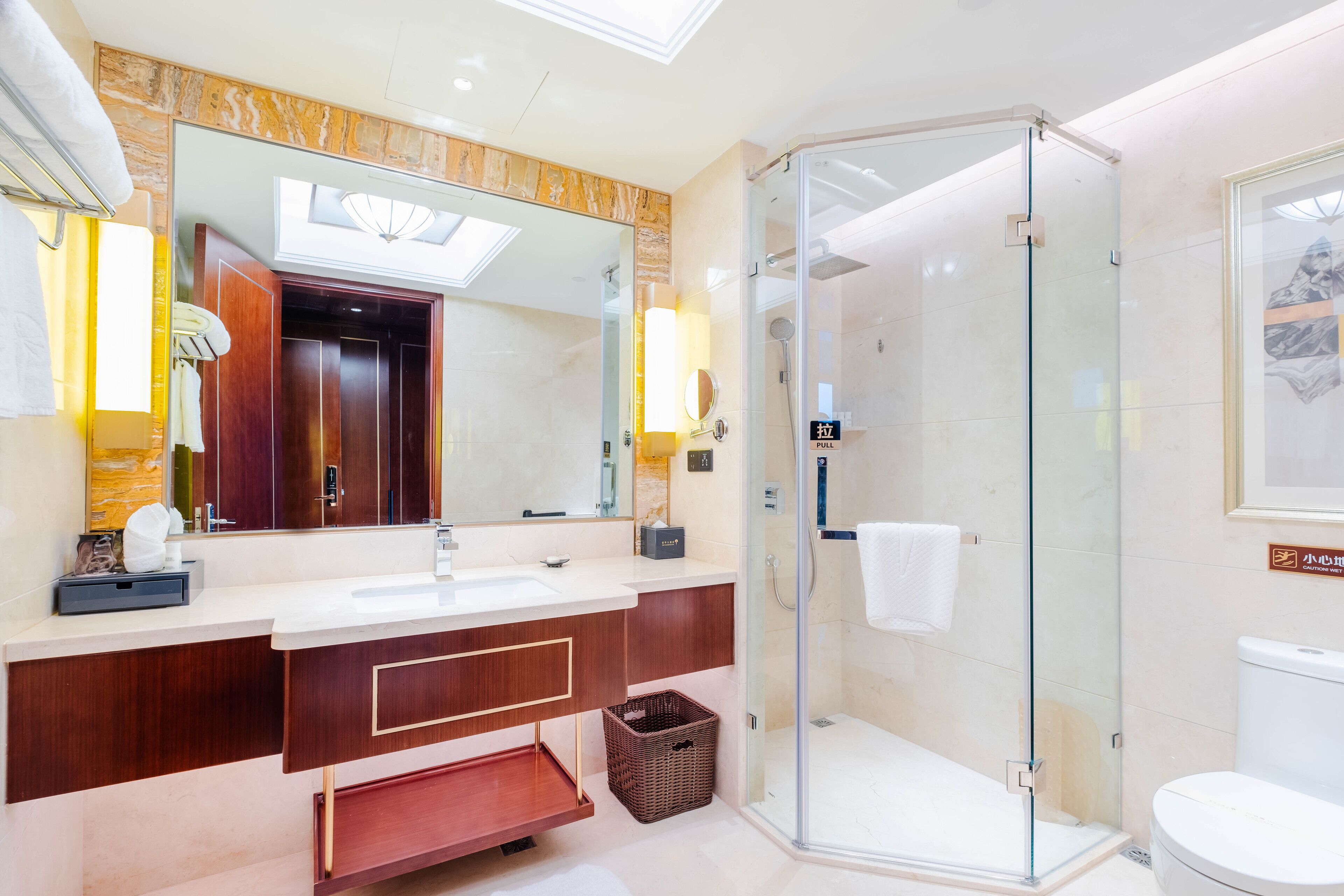 A modern bathroom with a glass-enclosed shower, a large mirror, and a marble countertop.