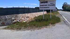 Schild für das Shadak Camping Village Restaurante mit einer Steinmauer und einem Zaun im Hintergrund.