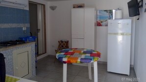 Eine kleine Küche mit einem Gasherd, einem Kühlschrank und einem weißen Schrank. Ein farbenfroher, gesteppter Sessel steht in der Mitte.