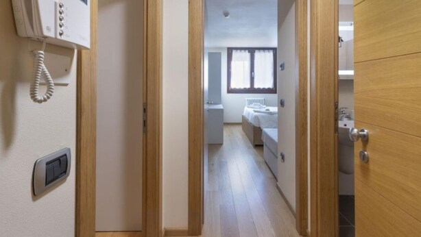 A narrow hallway leading to a bedroom with a bed, a radiator, and a window. - Acquaseria 310 in Ponte di Legno (Ponte di Legno)