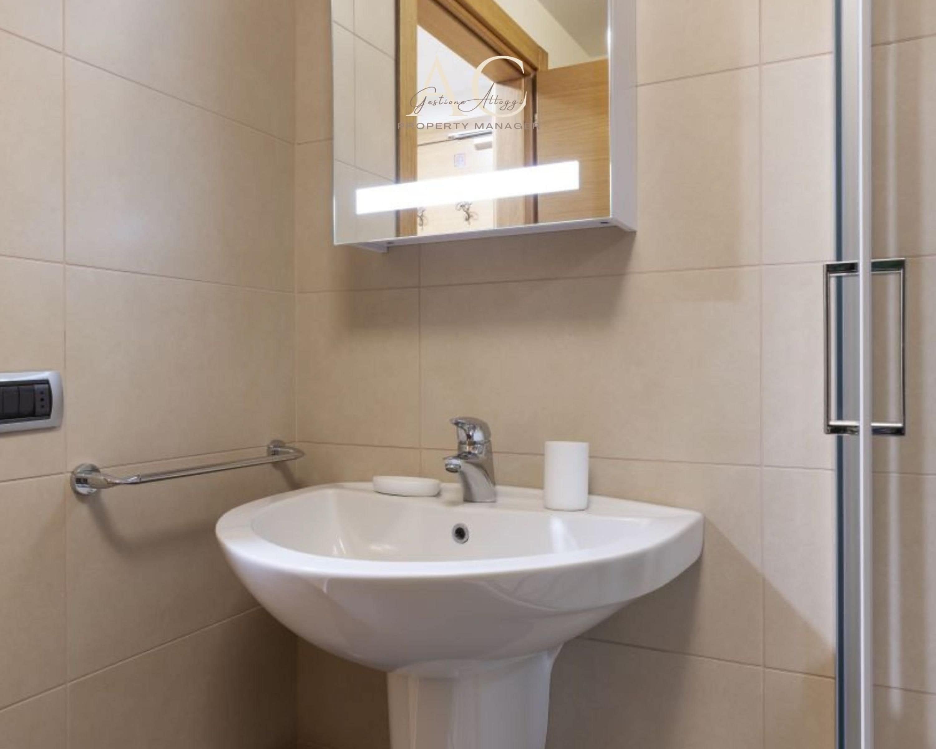 Een badkamer met een witte wasbak, een spiegel en een handdoekdispenser.