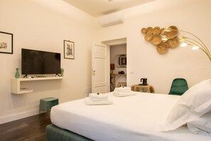 Un dormitorio moderno con una televisión de pantalla plana, una cama con toallas ordenadas, una silla verde y una decoración mural original.