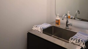 A bathroom with a sink, mirror, towel, soap dispenser, and pendant lights.