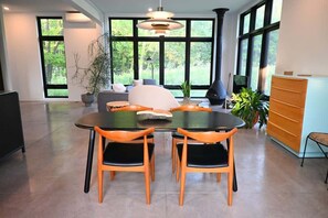 A modern dining area with a round table and chairs, a sofa, and a large window with a view of greenery. - NorthShore, Modern Cabin 656 (Northport)