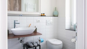 Une salle de bain moderne avec un lavabo blanc, un miroir, des toilettes et une étagère contenant des articles de toilette.